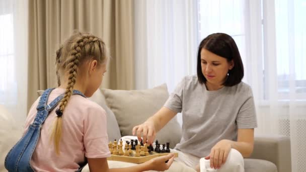 Mor och dotter spelar schack och sitter i soffa i vardagsrummet — Stockvideo