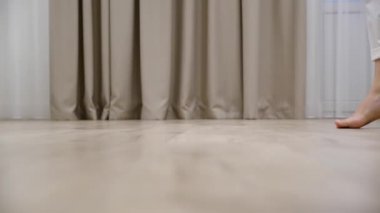 Genç bir kadın evdeki sıcak ahşap zeminde yalın ayak yürüyor.