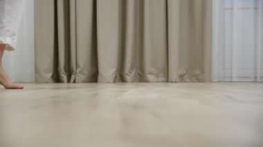 Genç bir kadın evdeki sıcak ahşap zeminde yalın ayak yürüyor.