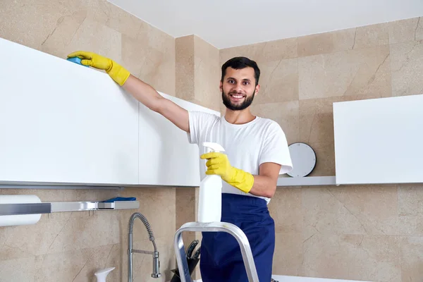 Hombre limpiando la superficie de la cocina en alto de pie en una escalera. Servicio de limpieza concepto —  Fotos de Stock