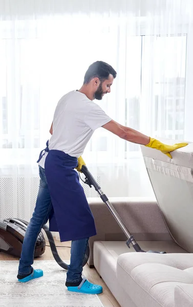Hombre joven Sofá de limpieza con aspiradora en la salida de la habitación en casa —  Fotos de Stock