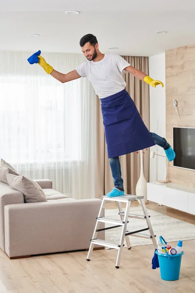 Adam tavanı temizlemek için merdivene tırmanırken eğleniyor. Temizlik hizmeti kavramı — Stok fotoğraf
