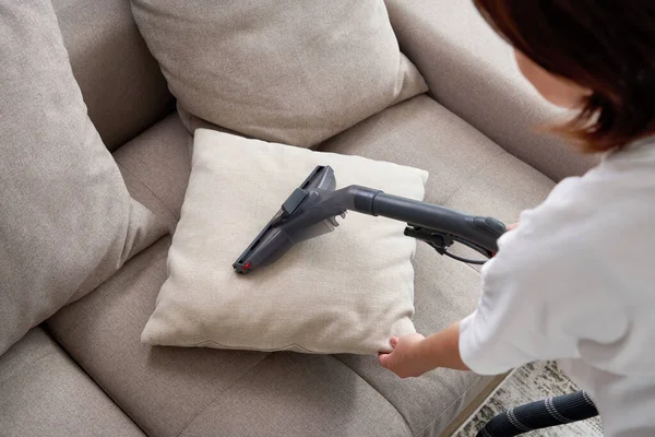 Junge Hausfrau putzt Sofa mit Staubsauger im Wohnzimmer — Stockfoto