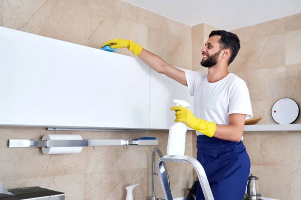 Hombre limpiando la superficie de la cocina en alto de pie en una escalera. Servicio de limpieza concepto —  Fotos de Stock