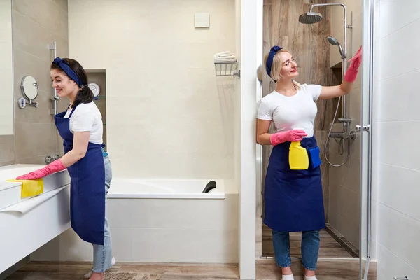 Дві жінки в уніформі стоять у ванній кімнаті. Концепція клінінгової служби — стокове фото