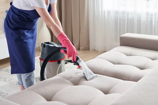 Женщина чистит диван с пылесосом дома. Концепция услуги уборки — стоковое фото