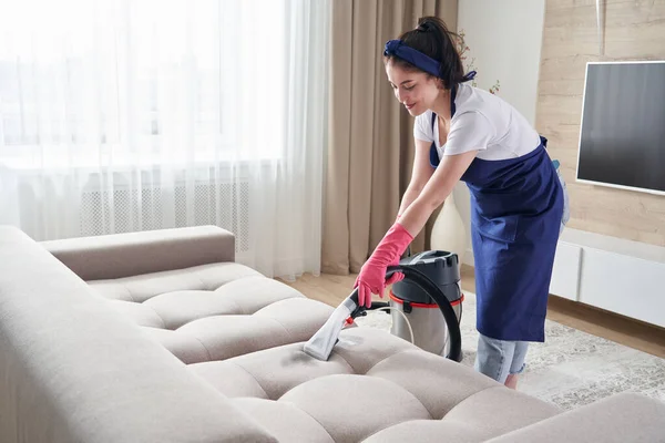 Woman cleaning couch with vacuum cleaner at home. Cleaning service concept — Stock Photo, Image