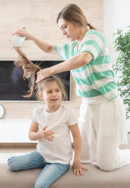 Mãe arrumar cabelos filhas. A rapariga não quer ter o cabelo escovado. foto de perto. criança se sente mal, porque a mãe puxa o cabelo — Fotografia de Stock