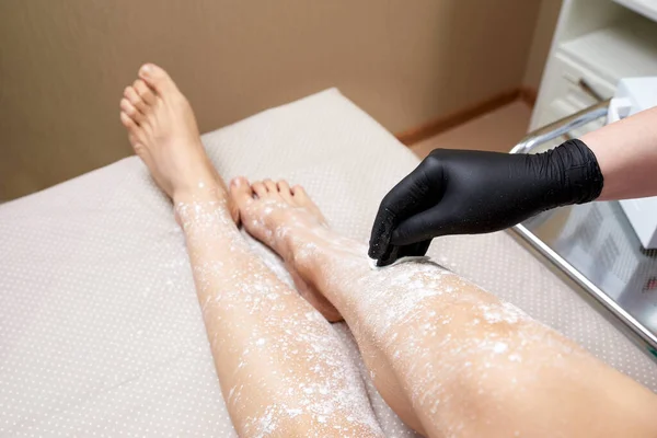 Kosmetyk przygotowuje się do woskowania kobiecych nóg w centrum spa. Przygotowanie do depilacji, nakładanie białego proszku — Zdjęcie stockowe
