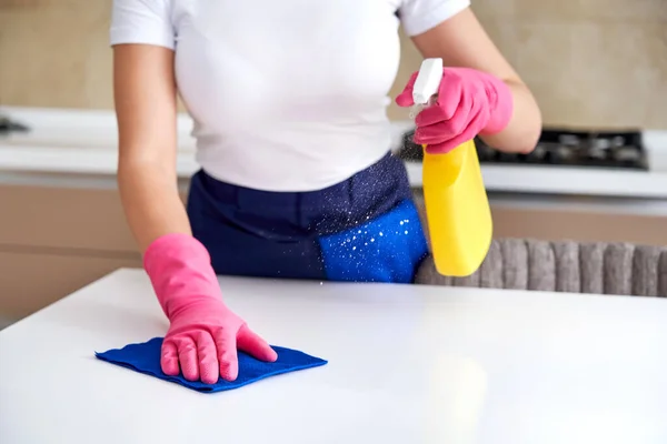 Жінка прибирає домашній стіл, дезінфікуючи поверхню кухонного столу з пляшкою з дезінфікуючим спреєм — стокове фото