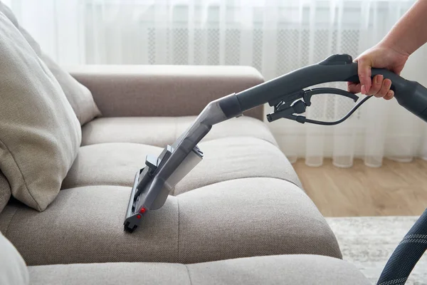 Junge Hausfrau putzt Sofa mit Staubsauger im Wohnzimmer — Stockfoto