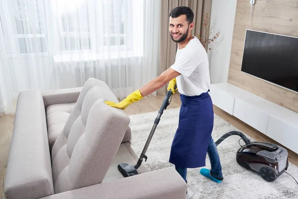 Young man Cleaning sofa With Vacuum Cleaner in leaving room At Home