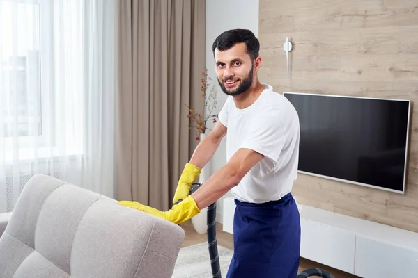 Młody człowiek Sprzątanie sofa z odkurzaczem w opuszczeniu miejsca w domu — Zdjęcie stockowe
