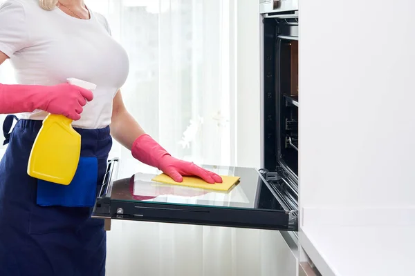 Молодая женщина в перчатках моет духовку на кухне. Концепция услуги уборки — стоковое фото