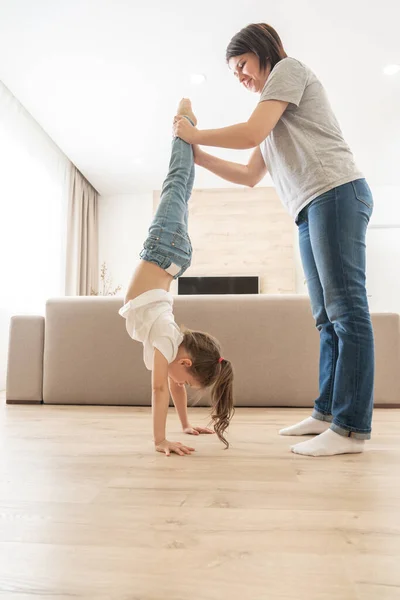 Moeder helpen dochter te lopen ondersteboven op haar armen thuis houden benen — Stockfoto