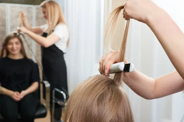 Hairstylist working on woman client with crimper — Stock Photo, Image