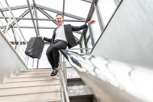 Feliz hombre de negocios con traje formal deslizándose por las escaleras Barandilla en el moderno edificio de negocios. Apúrate y concepto de libertad — Foto de Stock