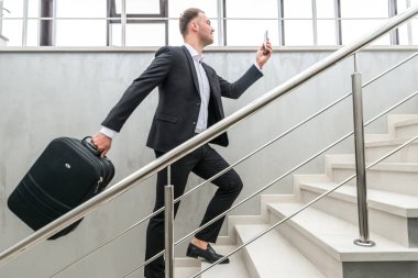Modern binada merdivenlerde koşan bir iş adamı bavulu tutuyor.