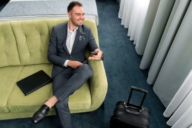 Neşeli iş adamı otel odasında bavuluyla iş gezisinde telefon kullanıyor.