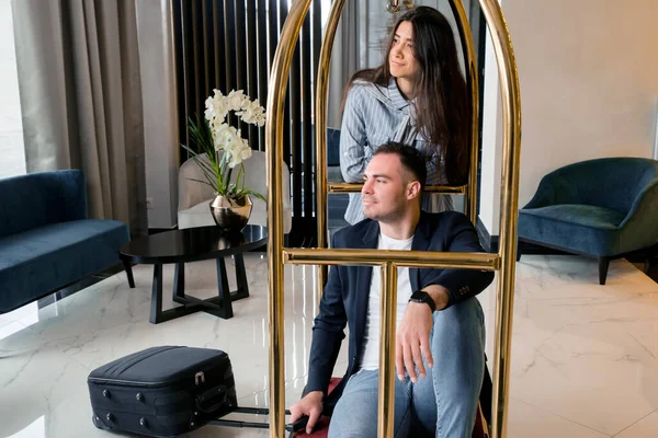 Mladý šťastný pár se baví tlačí hotel zavazadla vozík v hotelové hale — Stock fotografie