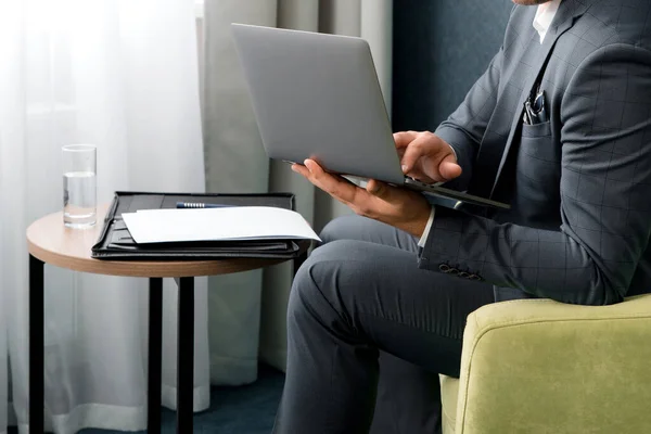 Joven hombre de negocios está utilizando el ordenador portátil mientras está sentado en la habitación del hotel — Foto de Stock