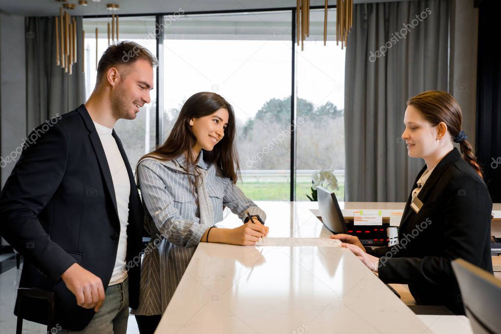 Couple and receptionist at counter in hotel. Young couple on a business trip doing check-in at the hotel