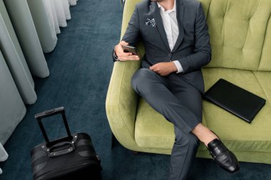 Neşeli iş adamı otel odasında bavuluyla iş gezisinde telefon kullanıyor.