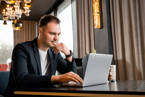 Joven hombre de negocios que trabaja en el ordenador portátil en la cafetería moderna en el hotel — Foto de Stock