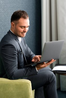 Genç yakışıklı iş adamı otel odasında dizüstü bilgisayarla çalışıyor.
