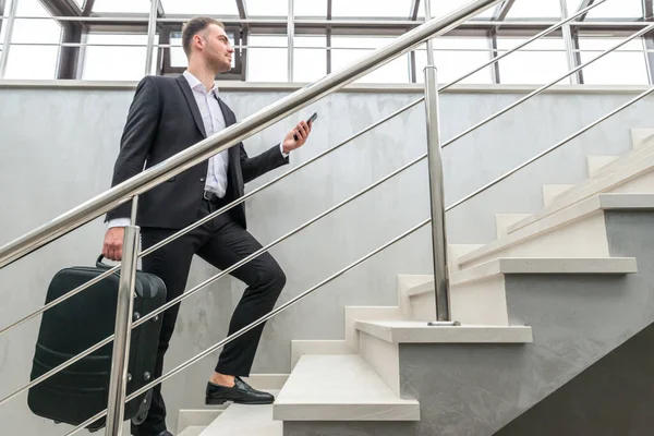 Empresario sosteniendo maleta corriendo en escaleras en edificio moderno — Foto de Stock