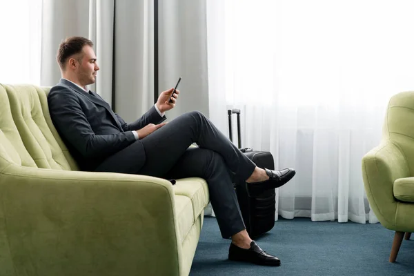Neşeli iş adamı otel odasında bavuluyla iş gezisinde telefon kullanıyor. — Stok fotoğraf