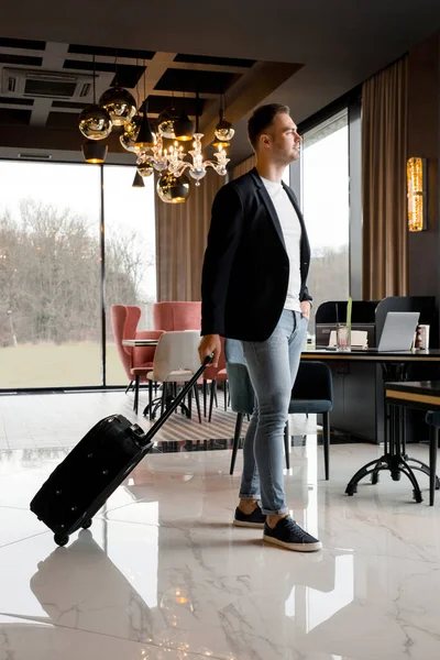 Seyahat çantalı genç adam modern otelin lobisinde yürüyor. — Stok fotoğraf