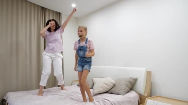 Щаслива молода мама і мила маленька дочка танцює, стрибає в ліжко, сміється мама грає з чудовою підлітковою дитиною в спальні, весела сімейна активність вдома, розважається — стокове відео