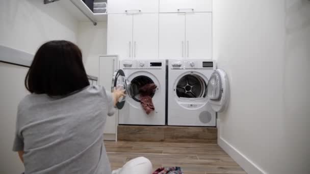 Młoda kobieta dobrze się bawiąc rzucając ubrania do pralki w pralni, zwolnione tempo Klip Wideo