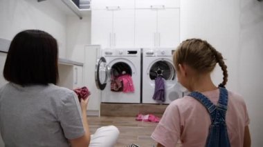 Genç kadın ve kızı evde çamaşır yıkarken çamaşır makinesine çamaşır atarken eğleniyorlar. Yavaş çekim