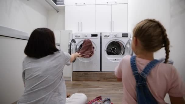 Jovem mulher e sua filha se divertindo enquanto lavava roupa em casa jogando roupas na máquina de lavar roupa. Movimento lento — Vídeo de Stock