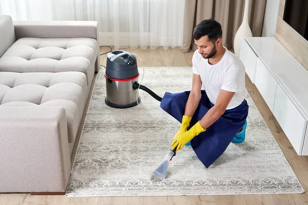Чоловік чистить килим у вітальні, використовуючи пилосос вдома. Концепція клінінгової служби — стокове фото