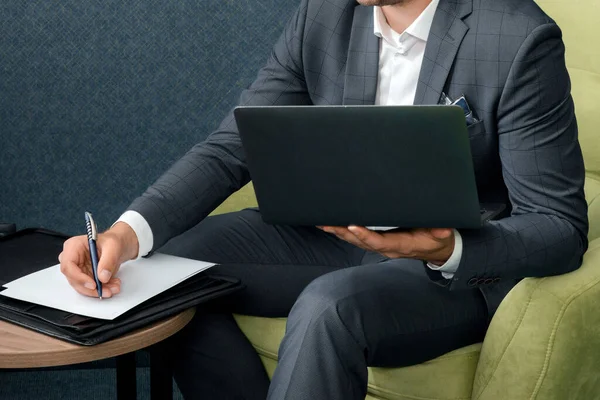 Joven hombre de negocios está utilizando el ordenador portátil y trabajando con documentos mientras está sentado en la habitación del hotel con la maleta. — Foto de Stock