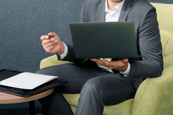 Il giovane uomo d'affari sta usando il computer portatile e sta lavorando con i documenti mentre è seduto nella stanza d'albergo con la valigia. — Foto Stock