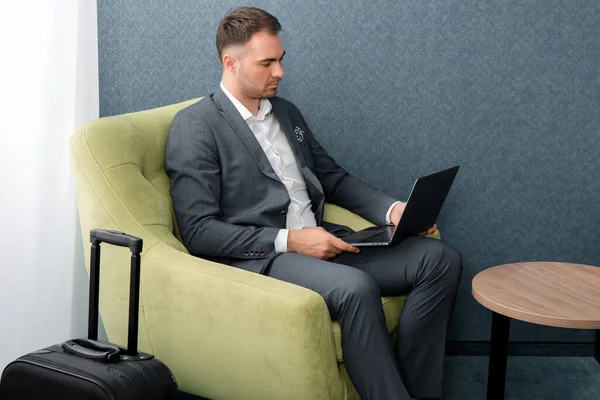 Joven hombre de negocios está utilizando el ordenador portátil mientras está sentado en la sala de negocios en el aeropuerto — Foto de Stock