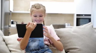 Çocuk evde oturma odasında kanepede dinlenirken tablet oynayıp müzik dinliyor.