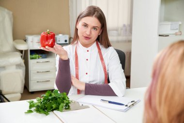 Beyaz üniformalı güzel bir beslenme uzmanı elinde kırmızı dolma biber tutuyor.