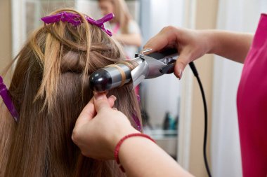 Kuaför, kuaförde uzun saçlı kuaför kız yapar. Saç maşasıyla bukleler oluştur