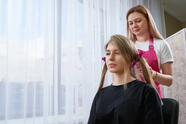 Fryzjer sprawia, że fryzjerka dziewczyna z długimi włosami w salonie piękności. Tworzenie loki z lokówki — Zdjęcie stockowe