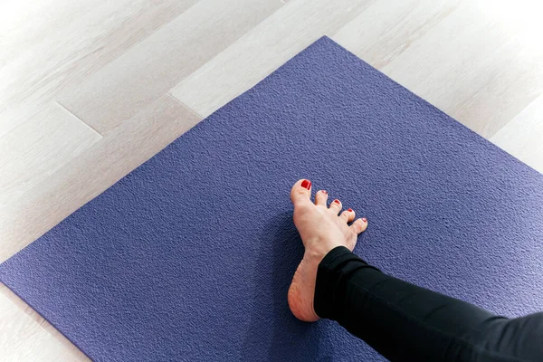 Женщина-йога растягивает ноги, раздвигая пальцы ног, делая растяжку на тренировочном коврике. — стоковое фото