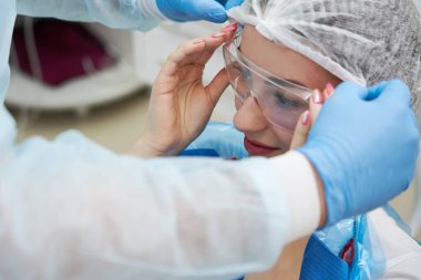 Diş hekimi, dişçilikte diş tedavisinden önce hasta kadına koruyucu gözlük takar.