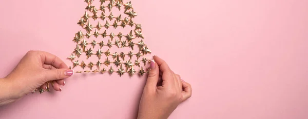 Flat lay of hands making golden christmas tree with star on pink paper — Stock Photo, Image