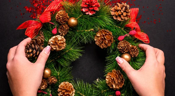 Female hands holding christmas wreath over black background with glitter and copy space — Stock Photo, Image
