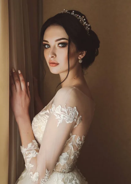 时尚图片 美丽的新娘 深色头发 穿着雅致的婚纱 头戴皇冠 早上在房间里摆姿势 — 图库照片