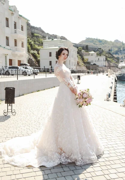 时尚的照片 美丽的新娘与深色的头发穿着优雅的婚纱摆在户外与招标花束 — 图库照片